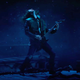 Eddie Munson shreds on his electric guitar in front of an ominously dark sky.